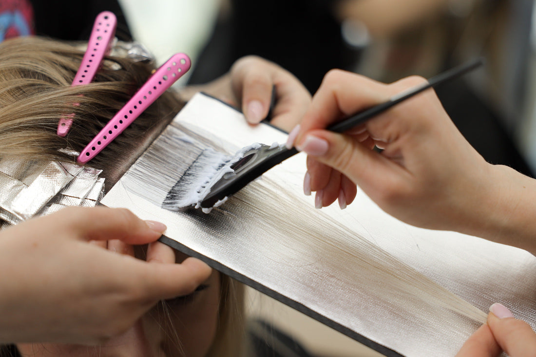 Colorist applying balayage hair color with brush using a carbon fiber board for clean, precise sections.